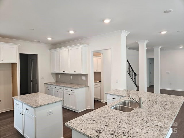8231 Annsborough Dr NW, Concord, NC 28027 - kitchen featuring an island with sink, dark wood-style flooring, white cabinetry, ornate columns, and light stone countertops