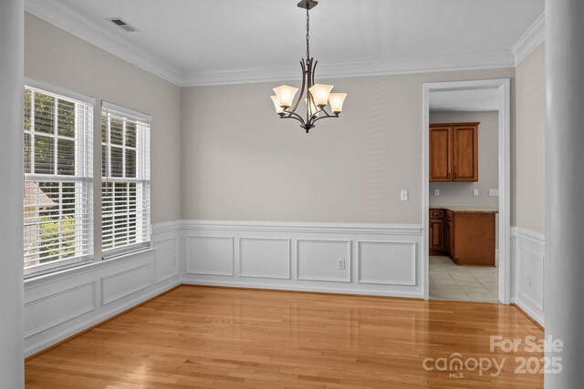 4519 Rock Stream Dr, Charlotte, NC 28269 - unfurnished dining area featuring plenty of natural light, light wood-type flooring, a chandelier, crown molding, and wainscoting