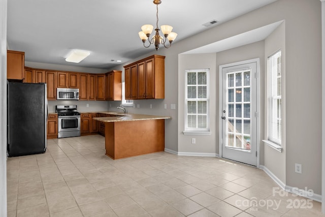 4519 Rock Stream Dr, Charlotte, NC 28269 - kitchen featuring appliances with stainless steel finishes, brown cabinetry, a chandelier, and healthy amount of natural light