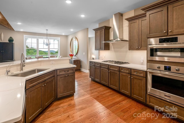 807 Hollybrook Dr, Flat Rock, NC 28731 - kitchen featuring wall chimney exhaust hood, light wood finished floors, stainless steel appliances, decorative backsplash, and a chandelier