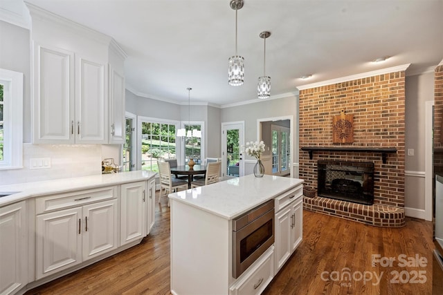 2317 Houston Branch Rd, Charlotte, NC 28270 - kitchen with stainless steel microwave, wood finished floors, white cabinetry, decorative light fixtures, and a brick fireplace