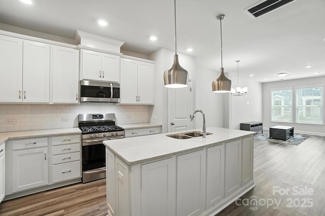 334 Ladybird Ln, Pineville, NC 28134 - kitchen with appliances with stainless steel finishes, wood finished floors, tasteful backsplash, white cabinets, and an island with sink