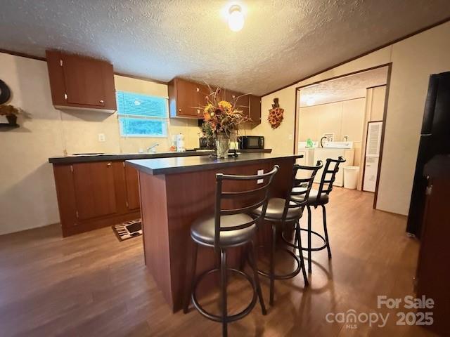 2418 6th Ave SW, Hickory, NC 28602 - kitchen with wood finished floors, a textured ceiling, dark countertops, a breakfast bar area, and brown cabinets