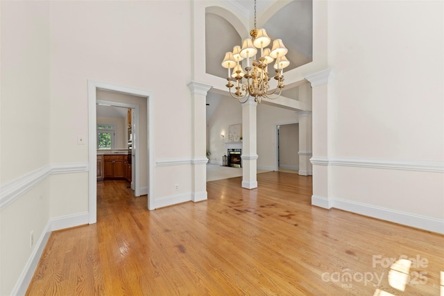 2241 Flagstick Dr, Matthews, NC 28104 - unfurnished dining area featuring a chandelier, decorative columns, light wood-type flooring, a lit fireplace, and a towering ceiling