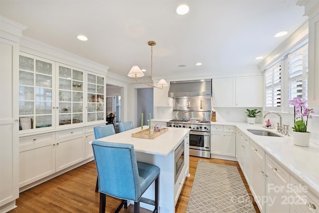 726 E Kingston Ave, Charlotte, NC 28203 - kitchen featuring wall chimney exhaust hood, appliances with stainless steel finishes, a center island, a kitchen breakfast bar, and white cabinetry