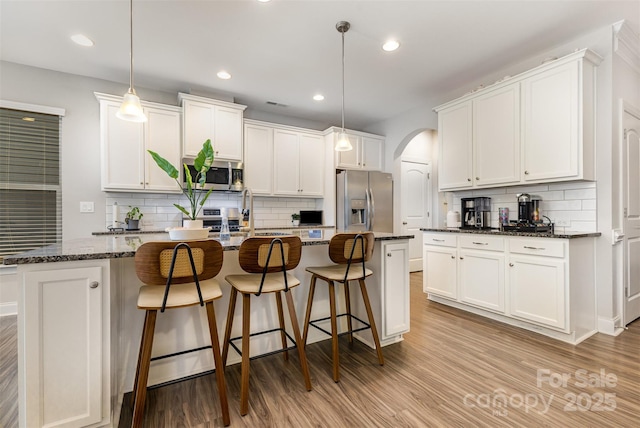 3332 Katherine Taylor Ct, Monroe, NC 28110 - kitchen featuring appliances with stainless steel finishes, tasteful backsplash, arched walkways, white cabinets, and light wood-style flooring