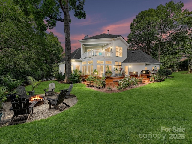 19205 Hidden Cove Ln, Cornelius, NC 28031 - back of house at dusk with a balcony, an outdoor fire pit, stucco siding, a yard, and a patio