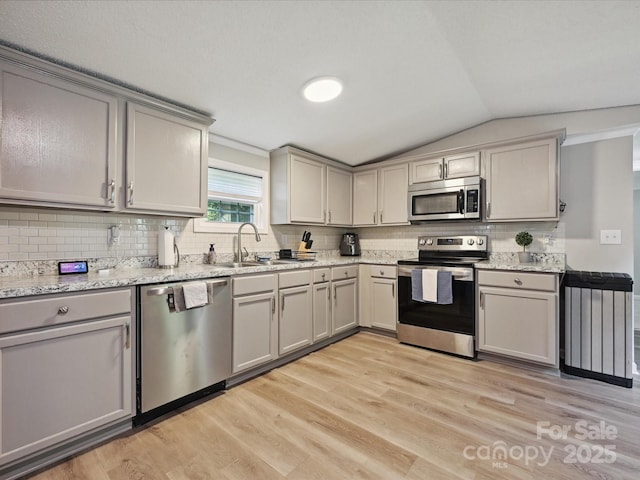 1140 Randall Ct, Concord, NC 28025 - kitchen with appliances with stainless steel finishes, lofted ceiling, gray cabinetry, light wood-type flooring, and decorative backsplash