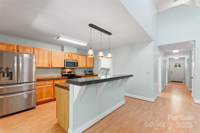 38 Live View Ln, Clyde, NC 28721 - kitchen featuring appliances with stainless steel finishes, dark countertops, light wood-style floors, a center island with sink, and a kitchen breakfast bar