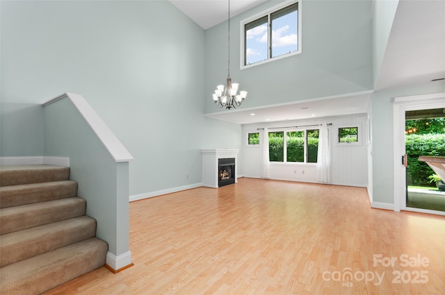 38 Live View Ln, Clyde, NC 28721 - unfurnished living room featuring a towering ceiling, a chandelier, light wood finished floors, stairs, and a warm lit fireplace