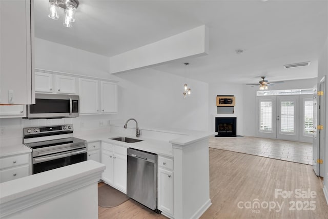 222 Ross Moore Ave, Charlotte, NC 28205 - kitchen featuring appliances with stainless steel finishes, a fireplace with flush hearth, white cabinets, light countertops, and a peninsula