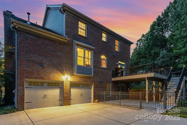 205 Rosedale Ln, Matthews, NC 28105 - back of house at dusk with a garage, brick siding, concrete driveway, stairway, and a deck