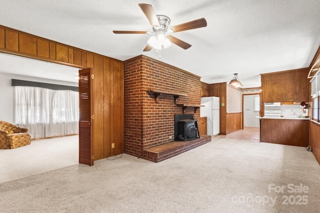 128 Howie St, Mount Holly, NC 28120 - unfurnished living room featuring wood walls, a wood stove, light colored carpet, a ceiling fan, and a textured ceiling