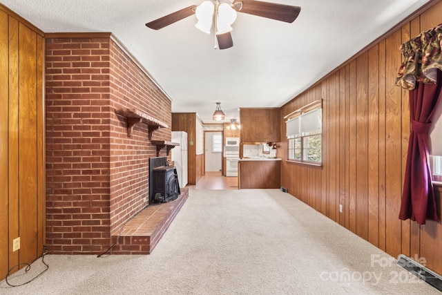 128 Howie St, Mount Holly, NC 28120 - unfurnished living room featuring a wood stove, carpet, wooden walls, and a ceiling fan