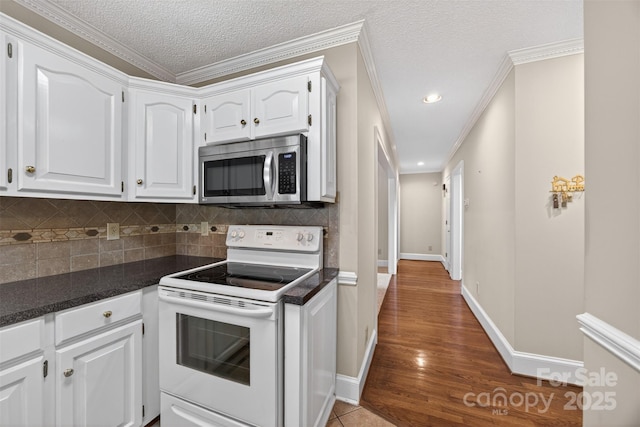 803 Woodmoore Ln, Kannapolis, NC 28081 - kitchen with stainless steel microwave, white range with electric cooktop, dark countertops, white cabinets, and decorative backsplash