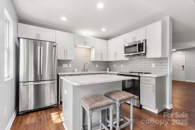 11023 Kinston Ridge Pl, Charlotte, NC 28273 - kitchen with stainless steel appliances, a center island, decorative backsplash, a breakfast bar, and dark wood-style flooring