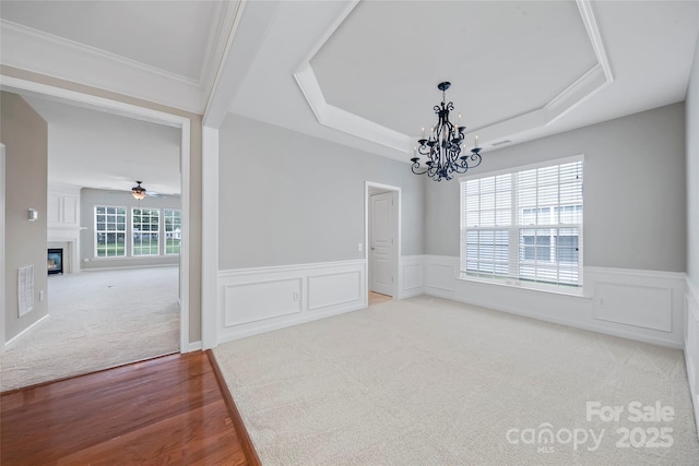 8409 Darcy Hopkins Dr, Charlotte, NC 28277 - spare room with a chandelier, a raised ceiling, a wainscoted wall, light wood-style flooring, and a glass covered fireplace