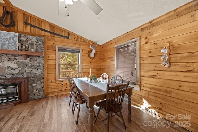 306 Forget Me Not Ln, Whittier, NC 28789 - dining area with lofted ceiling, wood walls, wood-type flooring, a ceiling fan, and a stone fireplace