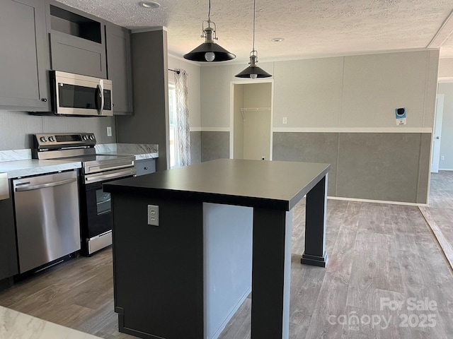 4180 Tallent Rd, Morganton, NC 28655 - kitchen with appliances with stainless steel finishes, wood finished floors, a textured ceiling, a kitchen island, and hanging light fixtures