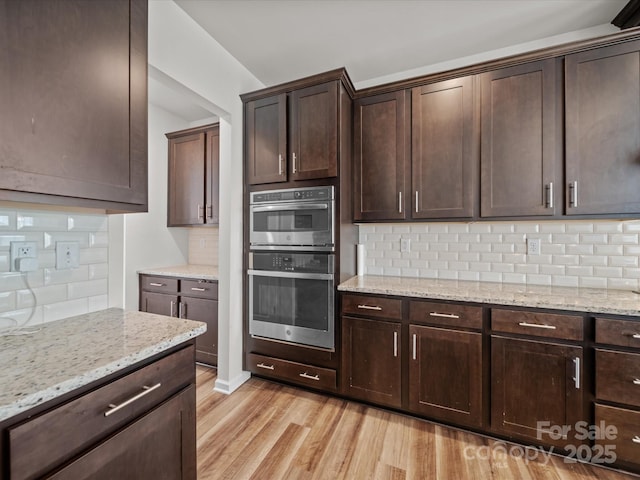 9582 Creighton Rd NW, Concord, NC 28027 - kitchen with stainless steel double oven, backsplash, light wood-type flooring, dark brown cabinets, and light stone countertops
