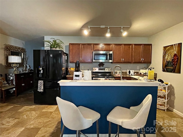 9608 Brackenview Ct, Charlotte, NC 28214 - kitchen with stainless steel appliances, rail lighting, brown cabinets, a kitchen breakfast bar, and light countertops