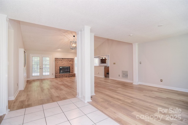 9117 Castle Garden Ln, Charlotte, NC 28215 - unfurnished living room with light wood-style floors, decorative columns, a textured ceiling, a brick fireplace, and french doors