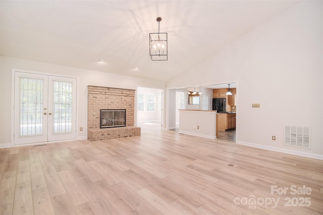 9117 Castle Garden Ln, Charlotte, NC 28215 - unfurnished living room with a chandelier, light wood-type flooring, french doors, a brick fireplace, and high vaulted ceiling