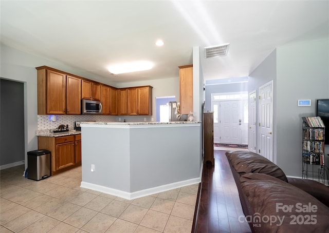 219 Harrowfield Hts, York, SC 29745 - kitchen featuring stainless steel microwave, brown cabinets, light stone countertops, decorative backsplash, and light tile patterned floors