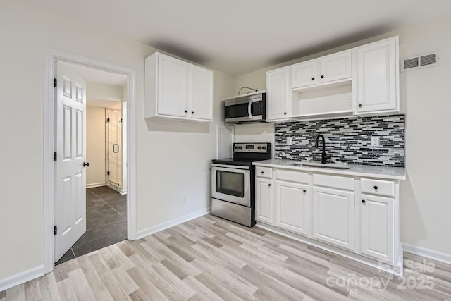 1224 E Woodlawn Rd, Charlotte, NC 28209 - kitchen featuring appliances with stainless steel finishes, light wood finished floors, tasteful backsplash, and white cabinets