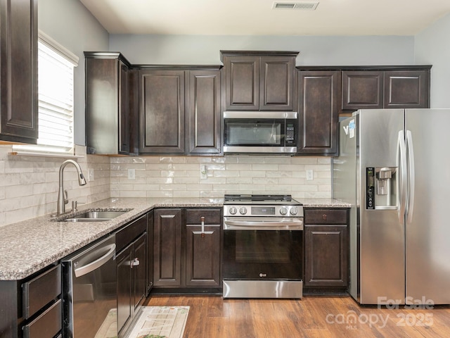 9123 Magnolia Lily Ave, Charlotte, NC 28227 - kitchen featuring appliances with stainless steel finishes, dark brown cabinetry, light stone counters, wood finished floors, and decorative backsplash