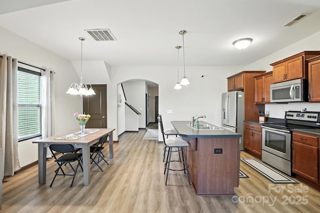 8152 Chilkoot Ln, Locust, NC 28097 - kitchen featuring appliances with stainless steel finishes, light wood-type flooring, dark countertops, arched walkways, and a breakfast bar