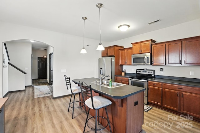 8152 Chilkoot Ln, Locust, NC 28097 - kitchen featuring stainless steel appliances, arched walkways, dark countertops, light wood-type flooring, and a breakfast bar