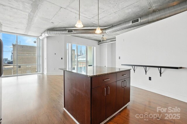 505 E 6th St Unit 908, Charlotte, NC 28202 - kitchen with wood finished floors, a kitchen island, dark stone countertops, dark brown cabinets, and hanging light fixtures
