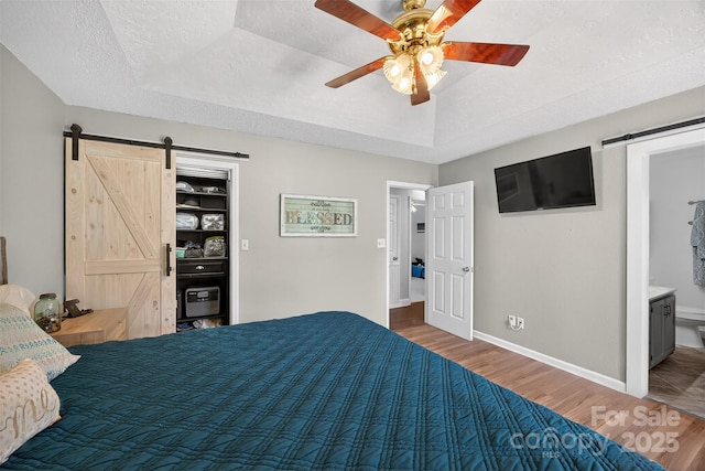 106 Abbey Cir, Salisbury, NC 28147 - bedroom featuring a barn door, wood finished floors, a tray ceiling, a textured ceiling, and connected bathroom