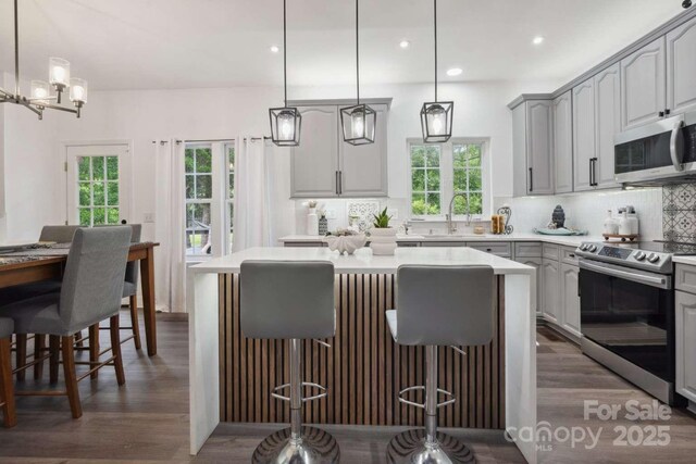 9954 Mitchell Glen Dr, Charlotte, NC 28277 - kitchen featuring stainless steel appliances, gray cabinets, dark wood-style floors, backsplash, and a center island