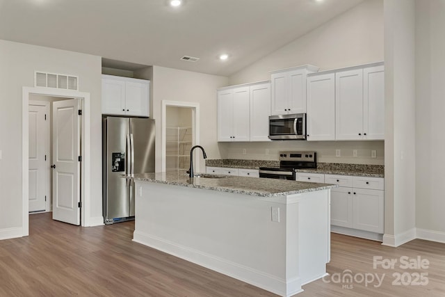 7106 Jerimoth Dr, Charlotte, NC 28215 - kitchen featuring stainless steel appliances, light wood-type flooring, white cabinetry, a center island with sink, and light stone counters
