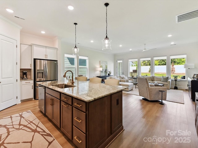 1120 Idyllic Ln, Waxhaw, NC 28173 - kitchen featuring white cabinets, light wood-style flooring, hanging light fixtures, light stone countertops, and an island with sink