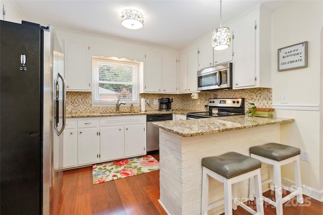 1219 Flowe Dr, Matthews, NC 28104 - kitchen featuring appliances with stainless steel finishes, a peninsula, dark wood-style flooring, decorative backsplash, and white cabinets