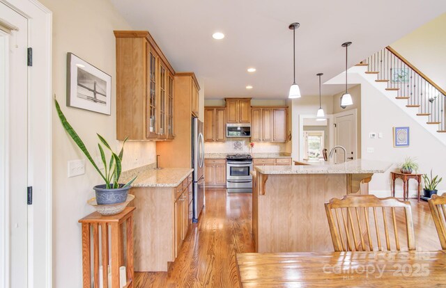 35 Village Pointe Ln, Asheville, NC 28803 - kitchen with stainless steel appliances, light wood finished floors, a kitchen breakfast bar, light stone countertops, and glass insert cabinets