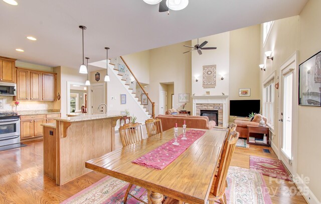 35 Village Pointe Ln, Asheville, NC 28803 - dining area with a ceiling fan, a stone fireplace, light wood-type flooring, stairway, and a towering ceiling
