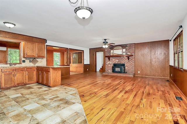 3311 Camden Rd, Marshville, NC 28103 - kitchen with wooden walls, a ceiling fan, brown cabinets, a brick fireplace, and light wood-style floors