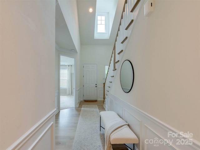 16108 Langston Dr, Charlotte, NC 28278 - hallway with a skylight, stairs, wainscoting, a decorative wall, and light wood-style flooring
