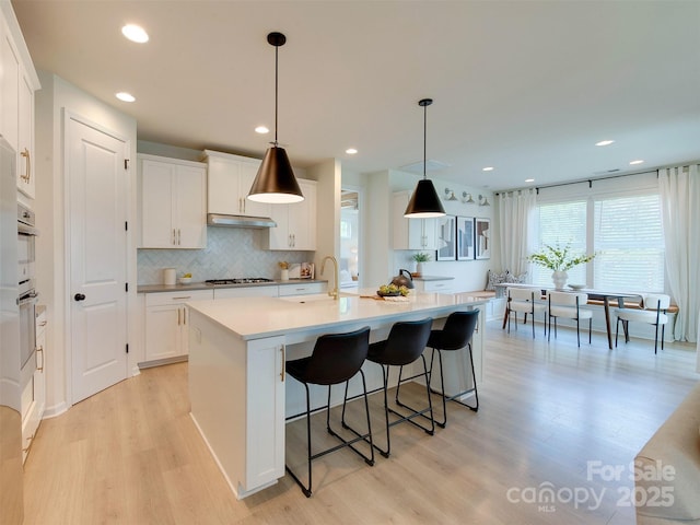 16108 Langston Dr, Charlotte, NC 28278 - kitchen with light wood-style floors, white cabinetry, a breakfast bar area, a kitchen island with sink, and recessed lighting