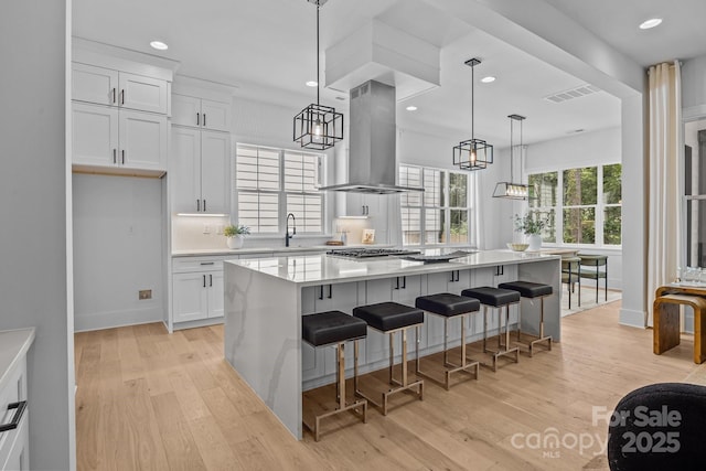 3949 Plainview Rd, Charlotte, NC 28208 - kitchen with wall chimney exhaust hood, a chandelier, light wood-style flooring, white cabinetry, and light countertops