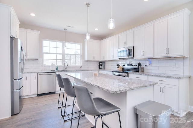 4017 Avis Way, Monroe, NC 28110 - kitchen featuring appliances with stainless steel finishes, a kitchen island, decorative backsplash, light wood finished floors, and white cabinets