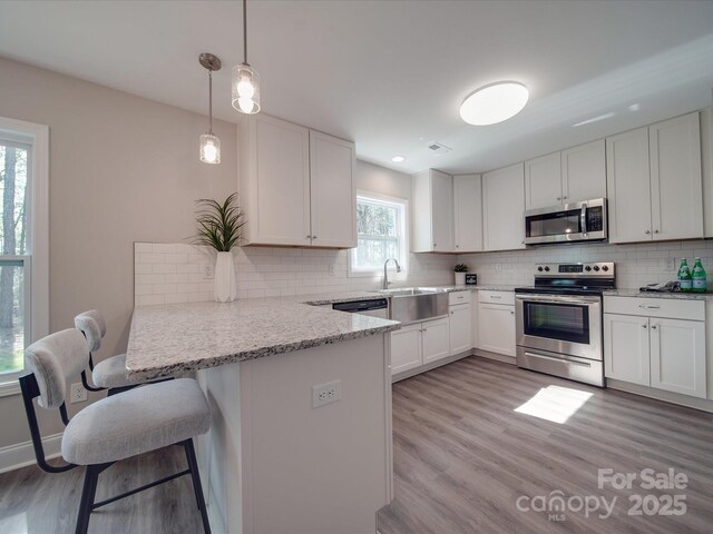 1016 Forest Dr, Marshville, NC 28103 - kitchen with stainless steel appliances, a peninsula, light wood-style flooring, tasteful backsplash, and white cabinets