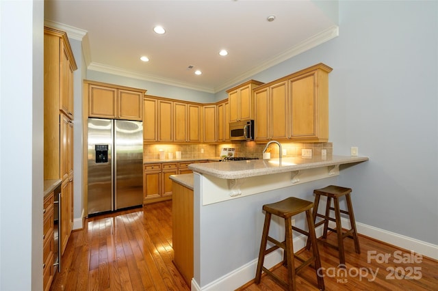6312 Mission Pl, Charlotte, NC 28210 - kitchen with stainless steel appliances, ornamental molding, a peninsula, decorative backsplash, and hardwood / wood-style floors