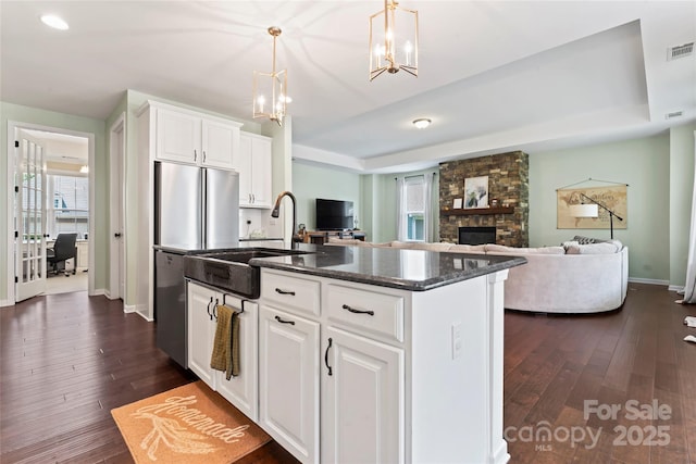 9547 Horsebit Ln, Concord, NC 28027 - kitchen with a tray ceiling, dark wood-style flooring, a center island with sink, and a stone fireplace