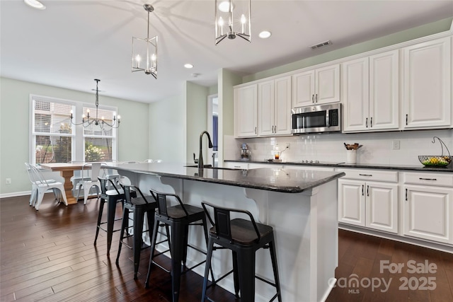 9547 Horsebit Ln, Concord, NC 28027 - kitchen featuring stainless steel microwave, a chandelier, decorative backsplash, dark wood finished floors, and white cabinets