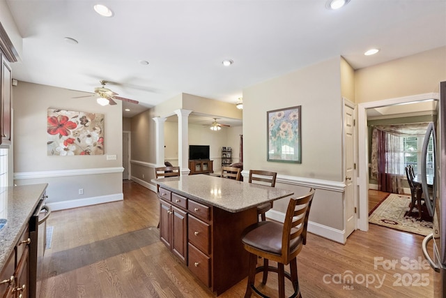 6309 Chamar Cir, Kannapolis, NC 28081 - kitchen featuring a ceiling fan, a kitchen breakfast bar, wood finished floors, ornate columns, and light stone counters